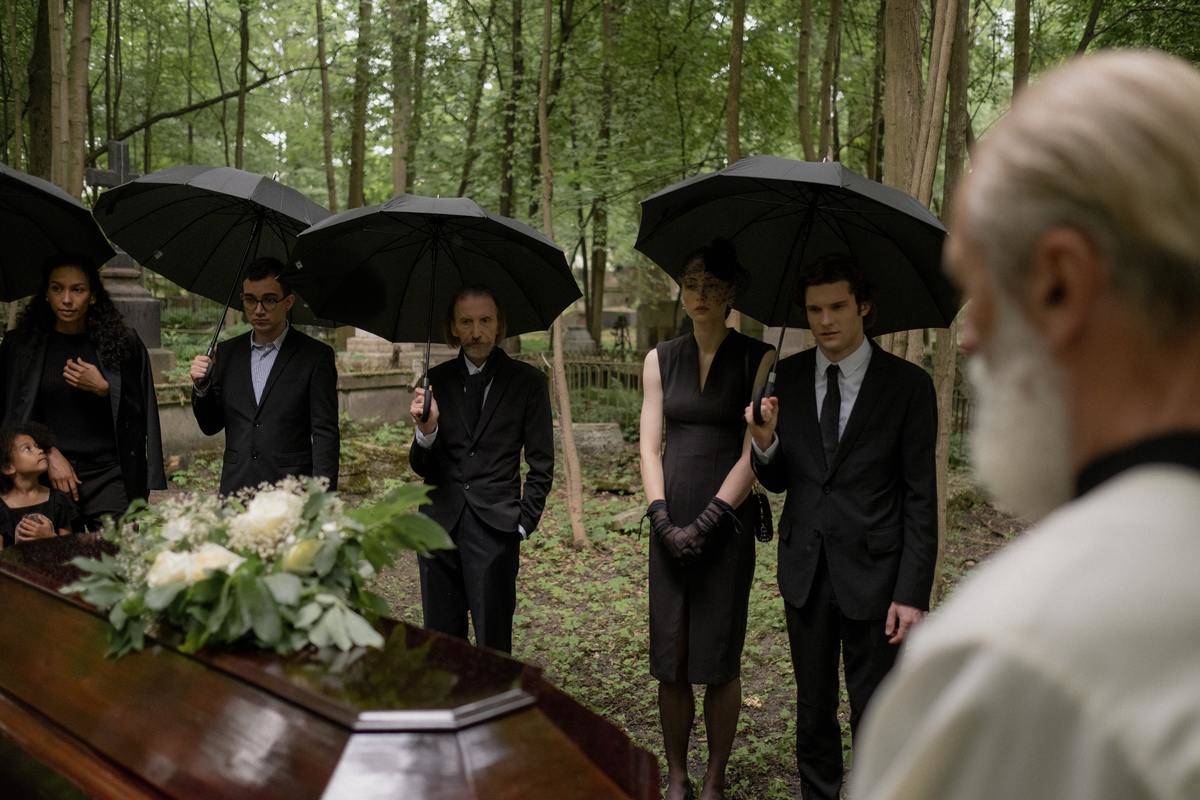 people standing under black umbrella by casket