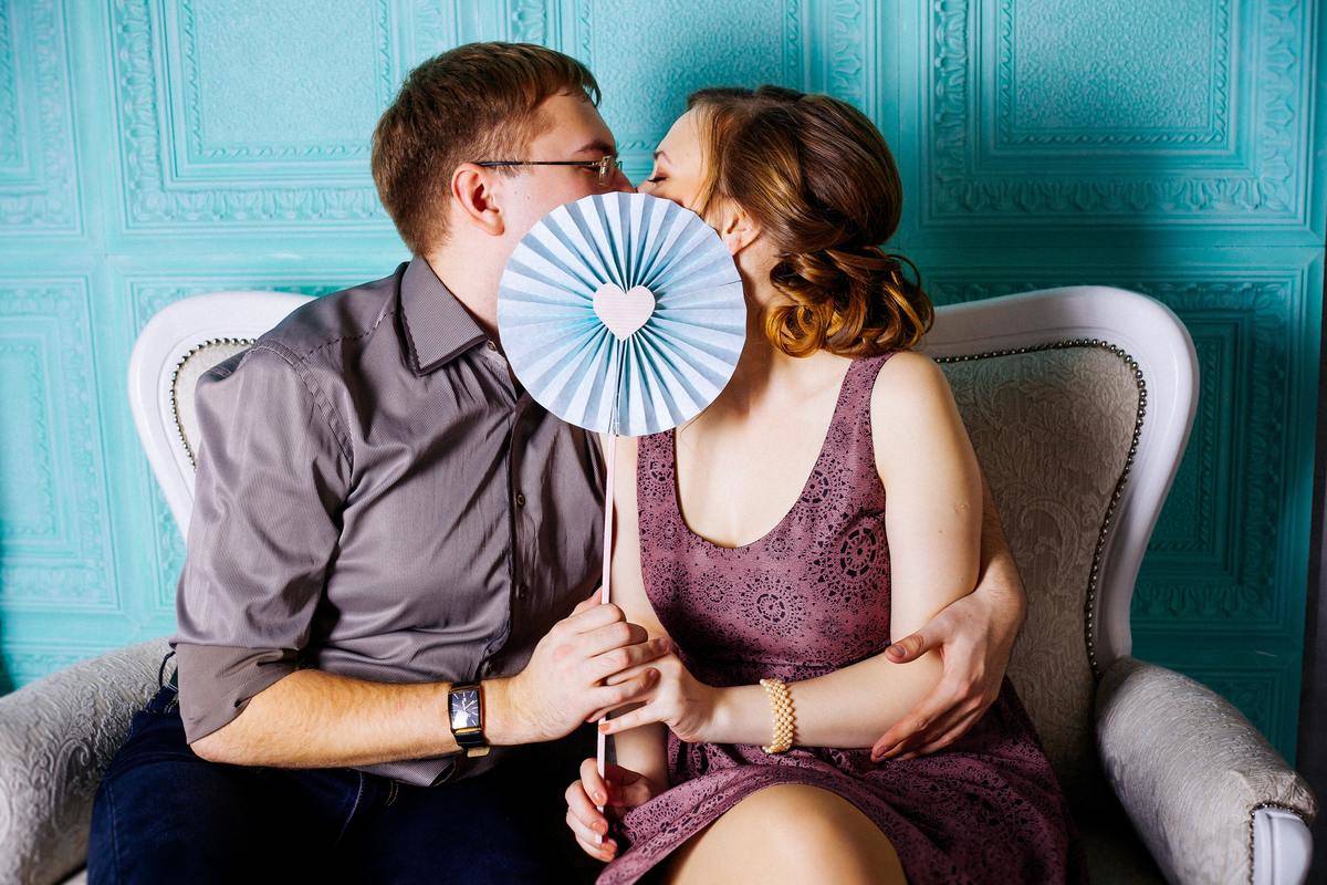 couple kiss behind paper fan by blue wall on couch