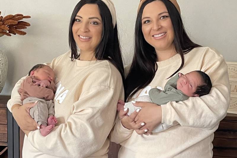 twin sister hold babies in matching outfits