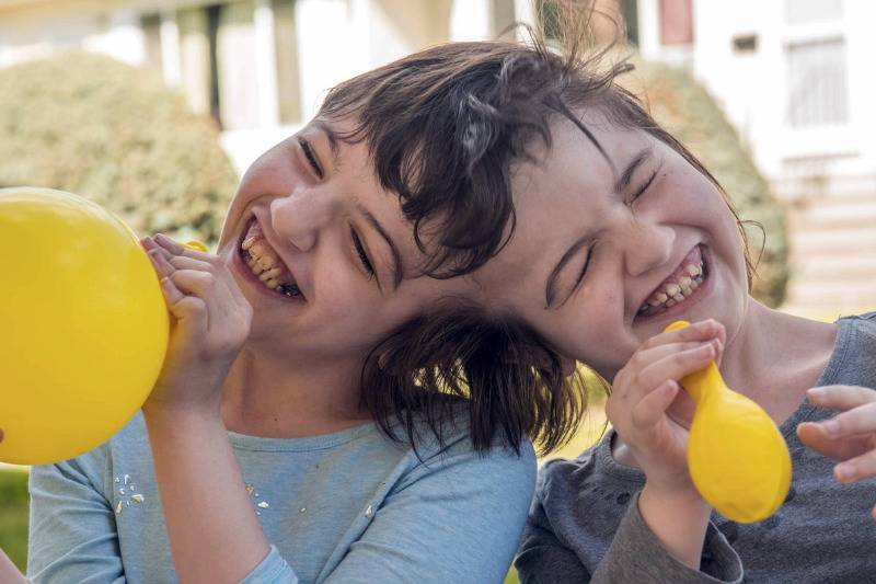 twins laughing while blowing yellow balloons