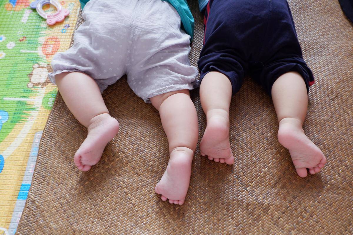close up of two babies on carpet from the back on their feet
