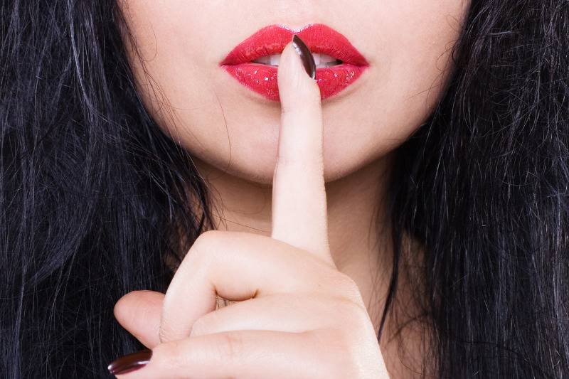 woman holds finger to her red lips in 
