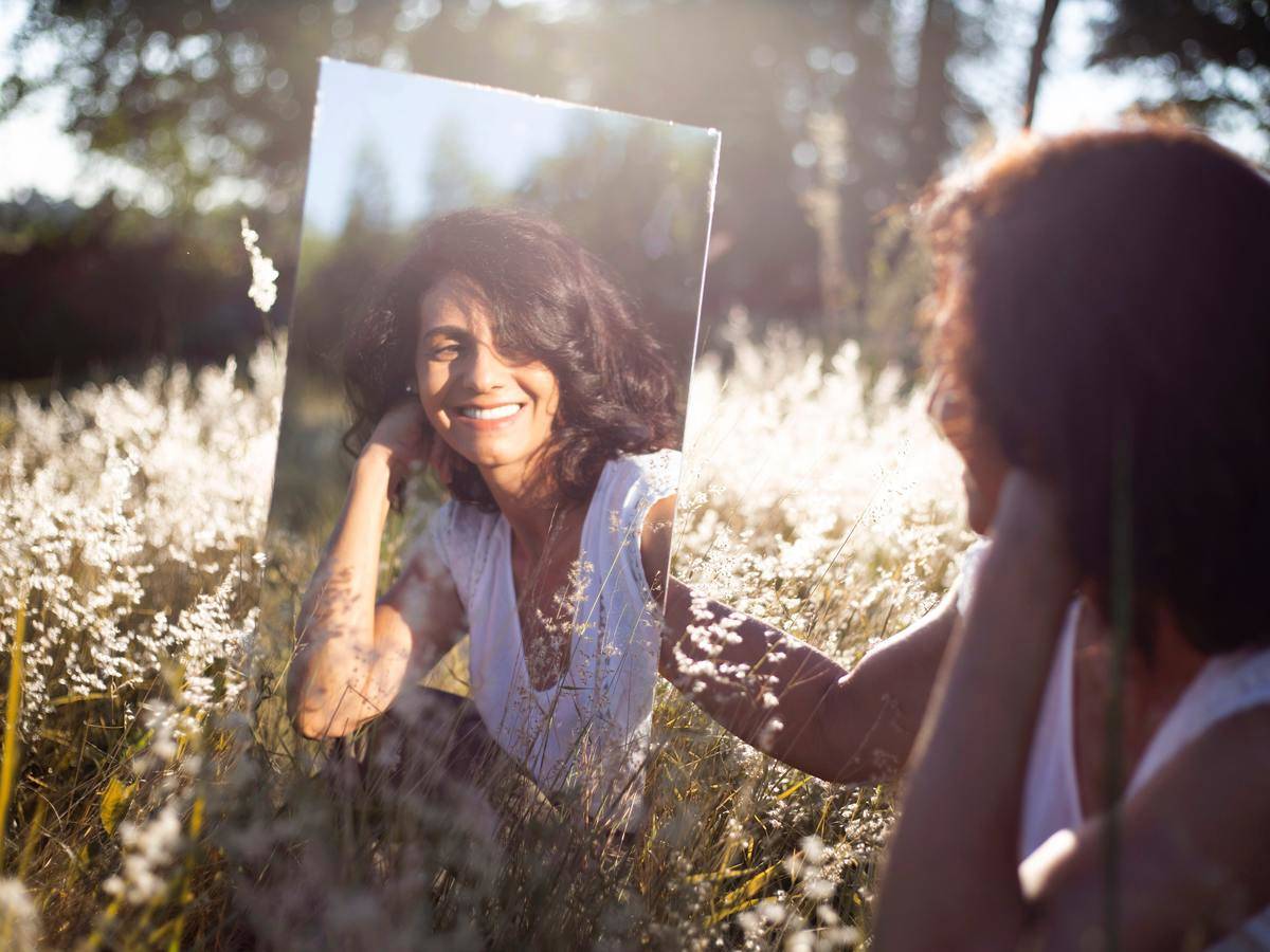 woman looking in the mirror smiling at herself in a field