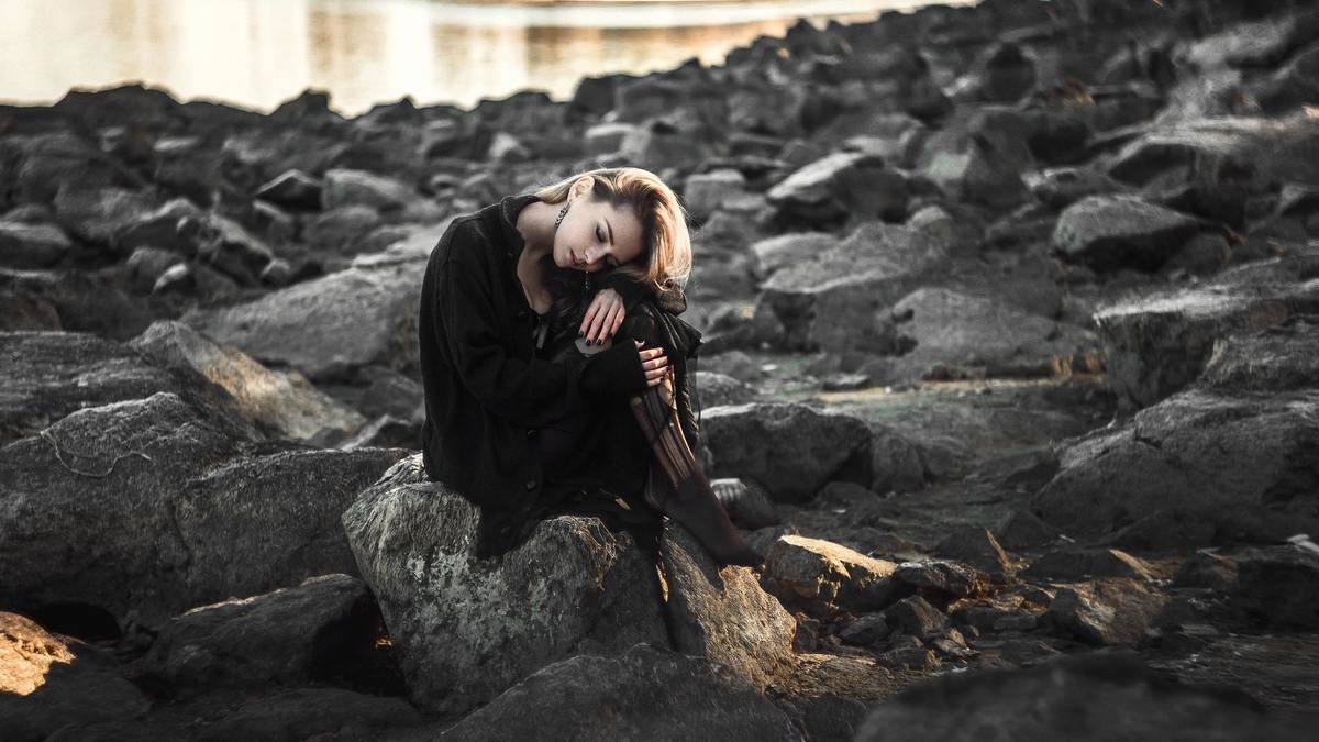 woman sitting on rocks while hugging in her knees