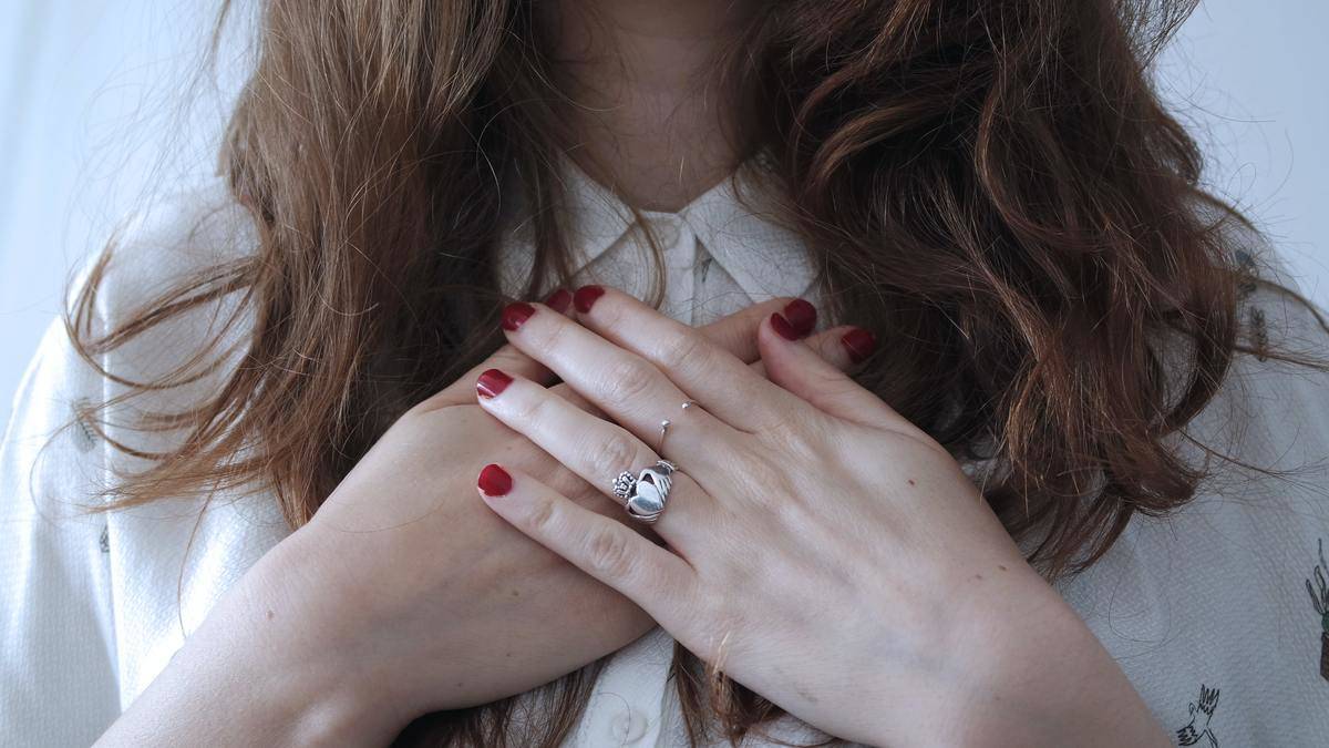 close up woman rests her hands on her heart