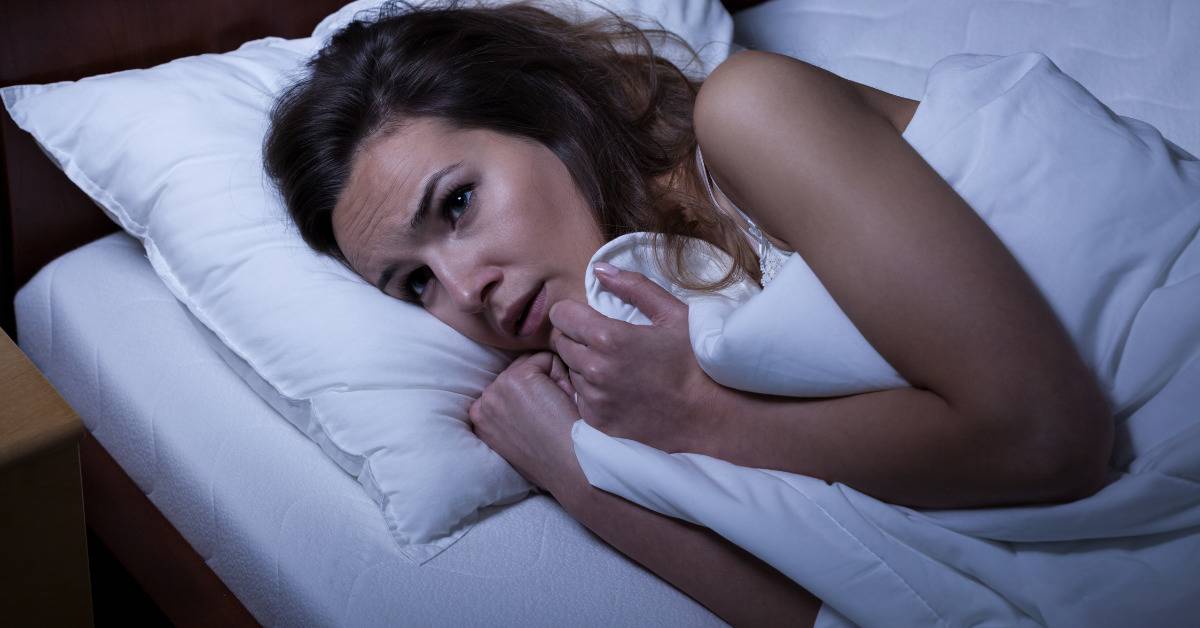 woman scared in bed clenching to the sheets