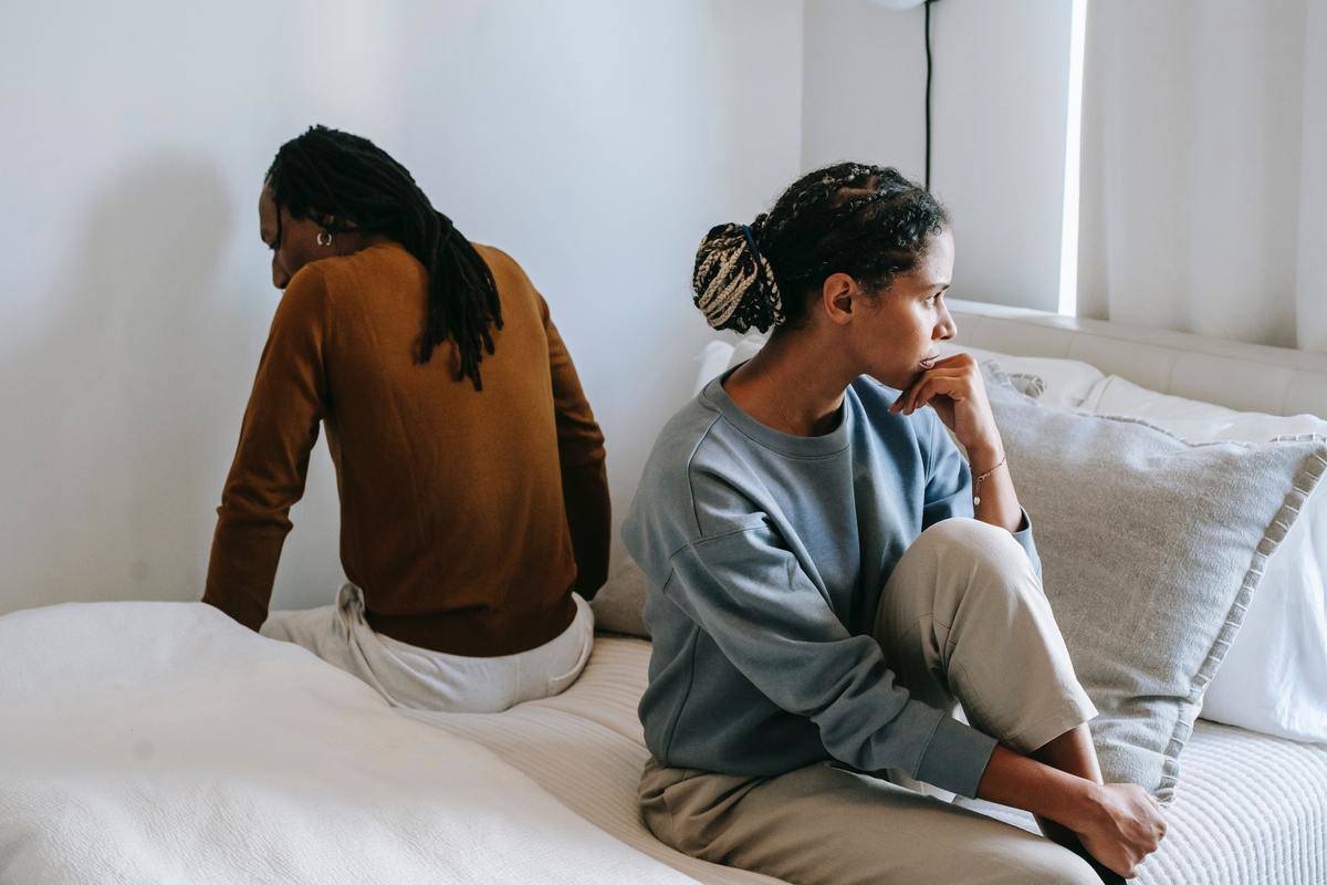 woman sits on bed across man 