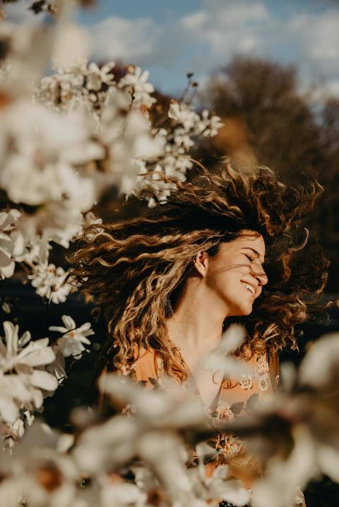 woman with curly hair flipping it surrounded by flowers