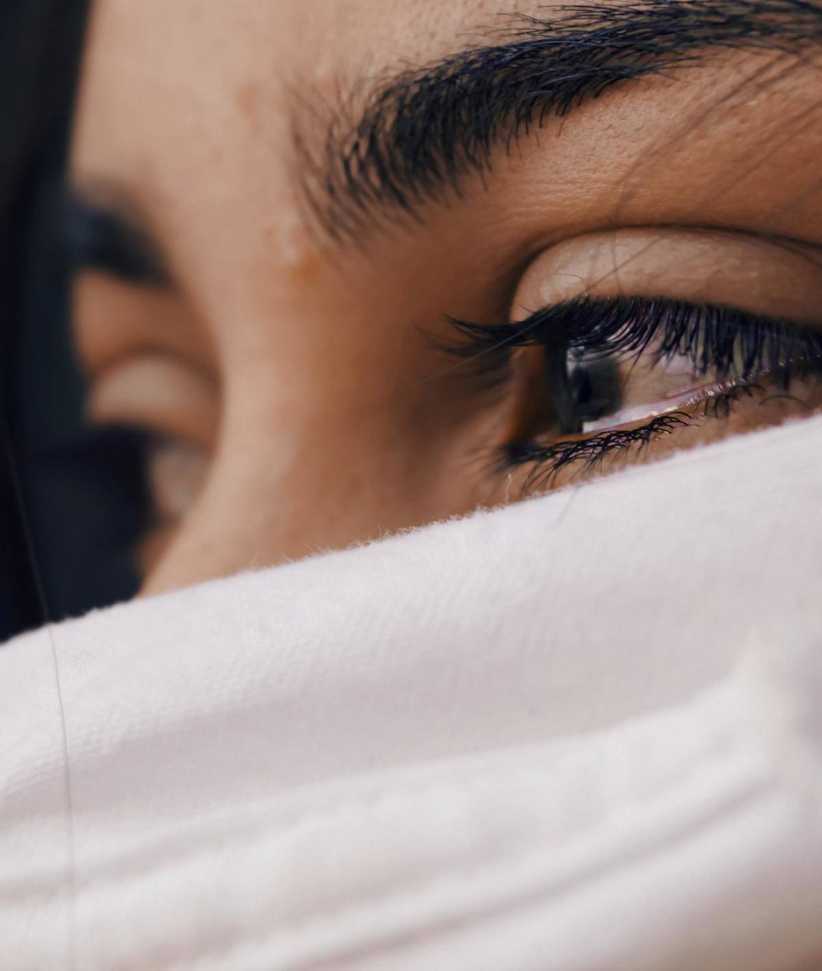 close up of woman with tears in her ad face hidden in white scarf eyesl