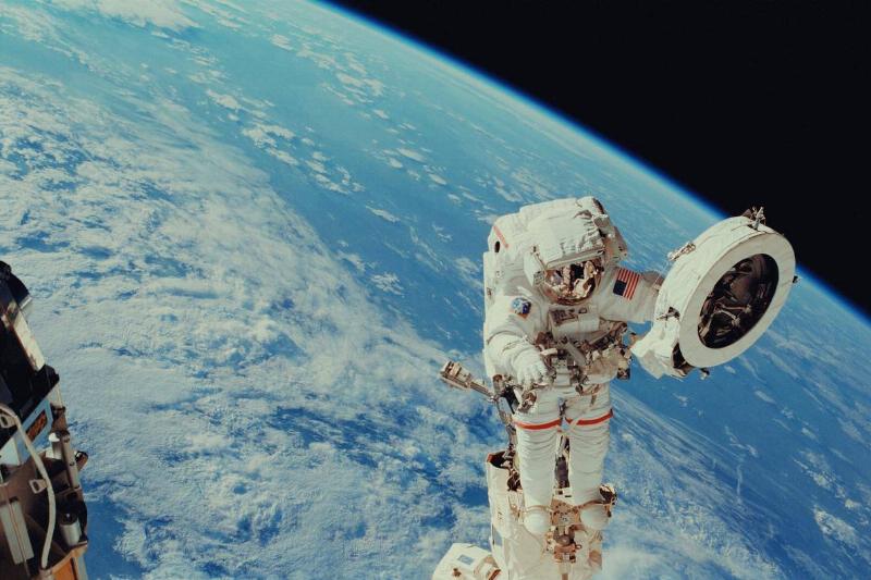 An astronaut floating above planet Earth holding space technology.