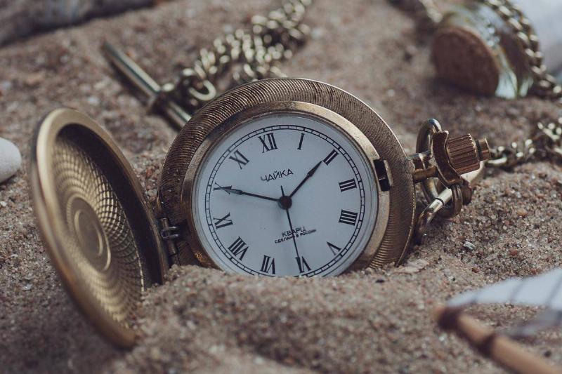 A locket-style clock sitting in a pile of sand.