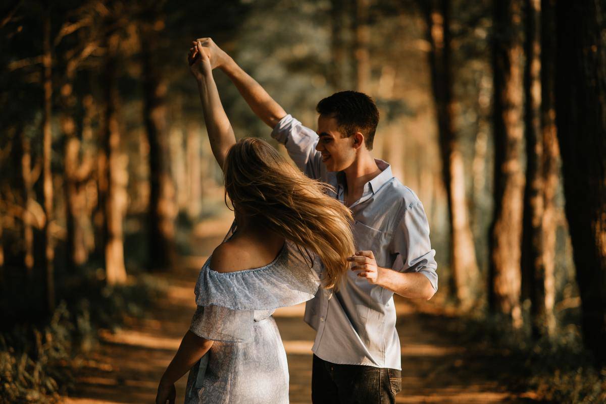 A young couple dancing in a forest, their arms raised in a twirl.