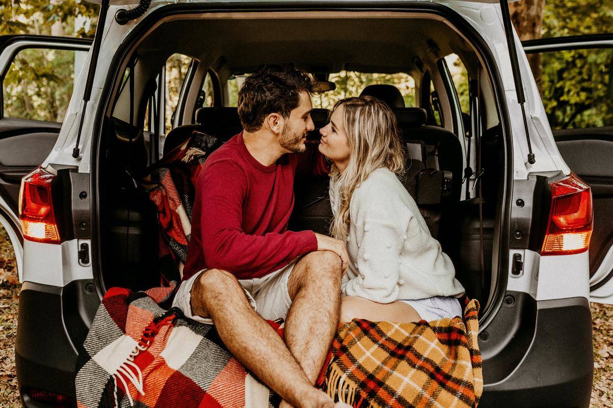 A young couple sitting on blankets in an open SUV trunk.