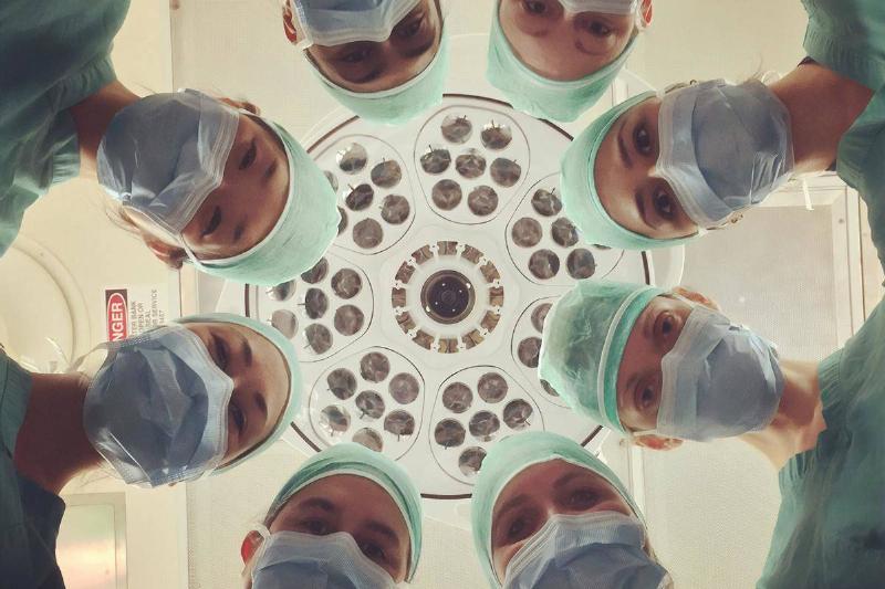 A group of doctors and nurses wearing hospital gowns and masks looking down at a patient.