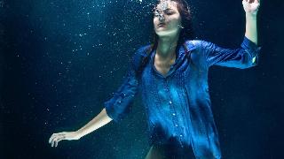 A woman in a blue button-up shirt drowning in deep blue water.