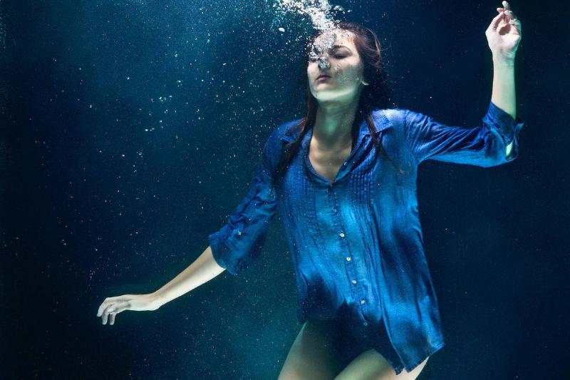 A woman in a blue button-up shirt drowning in deep blue water.