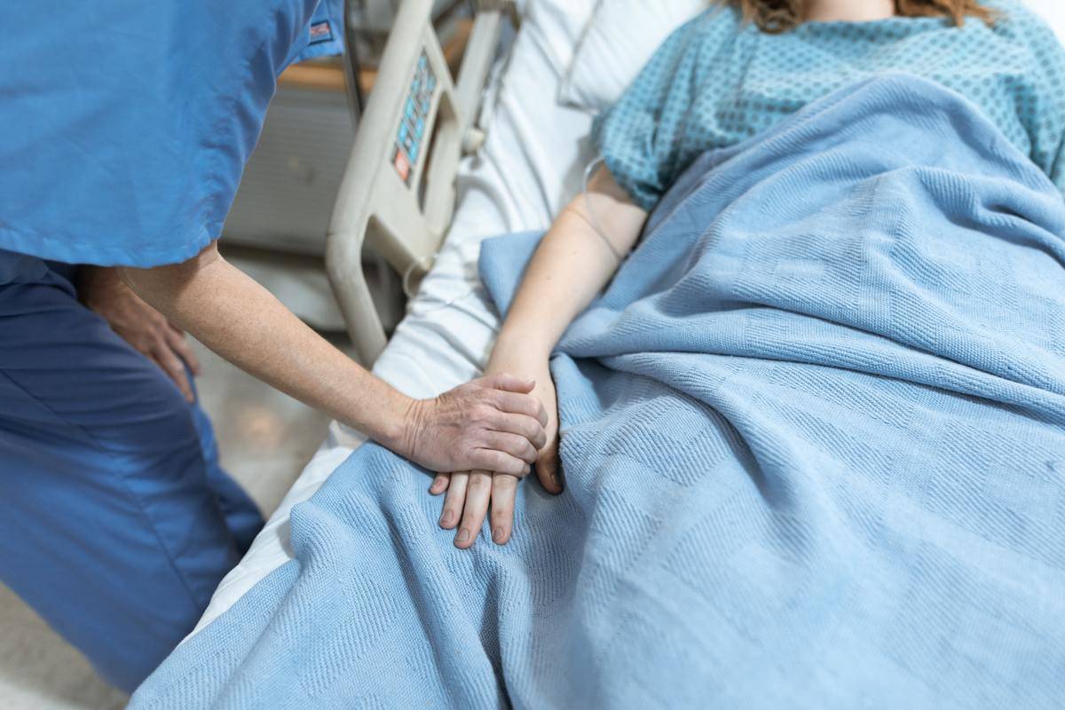 A nurse holding the hand of a hospital patient.