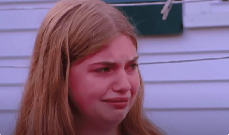 A young girl crying in front of a white trailer.