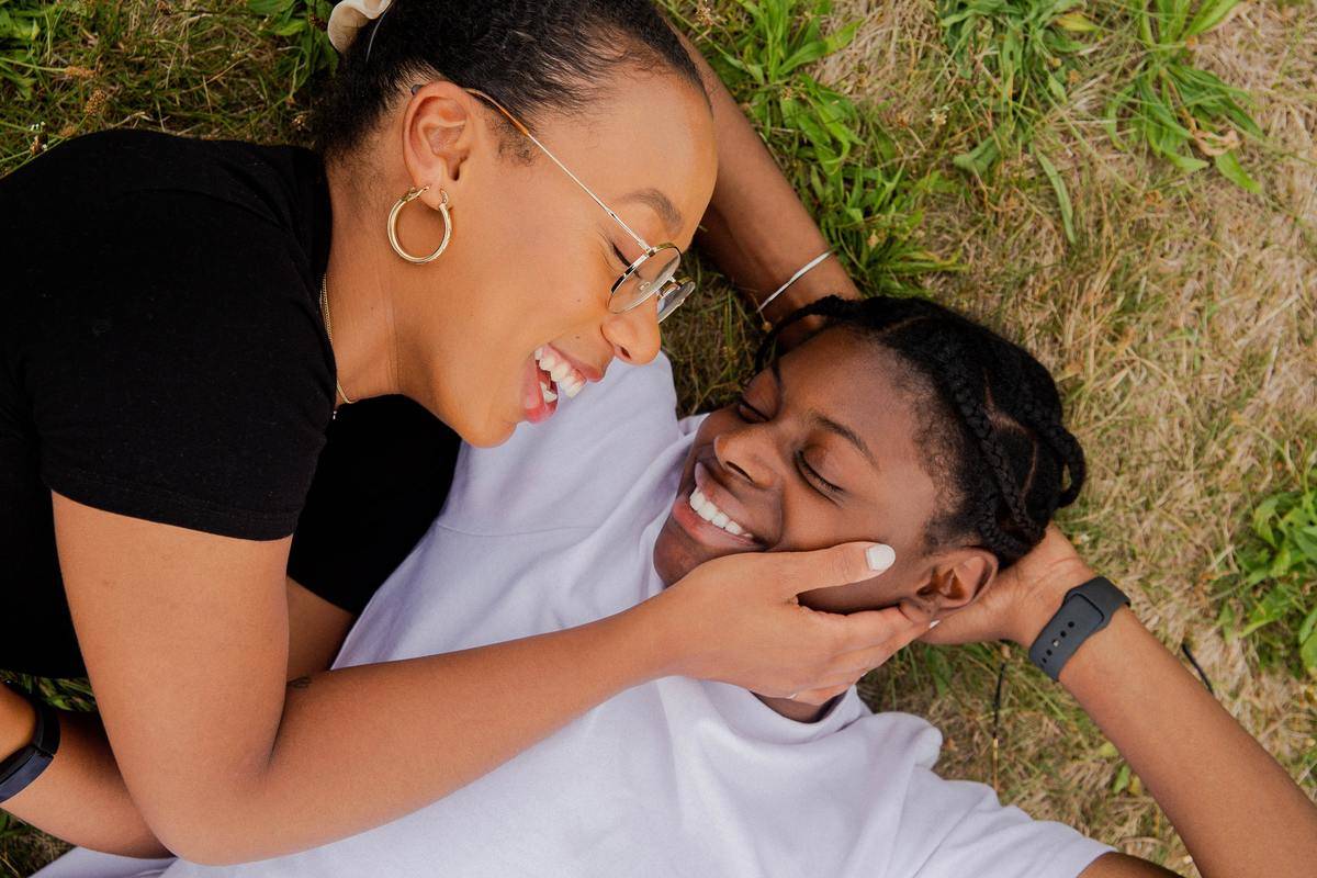 A young couple laying together in the grass, laughing.