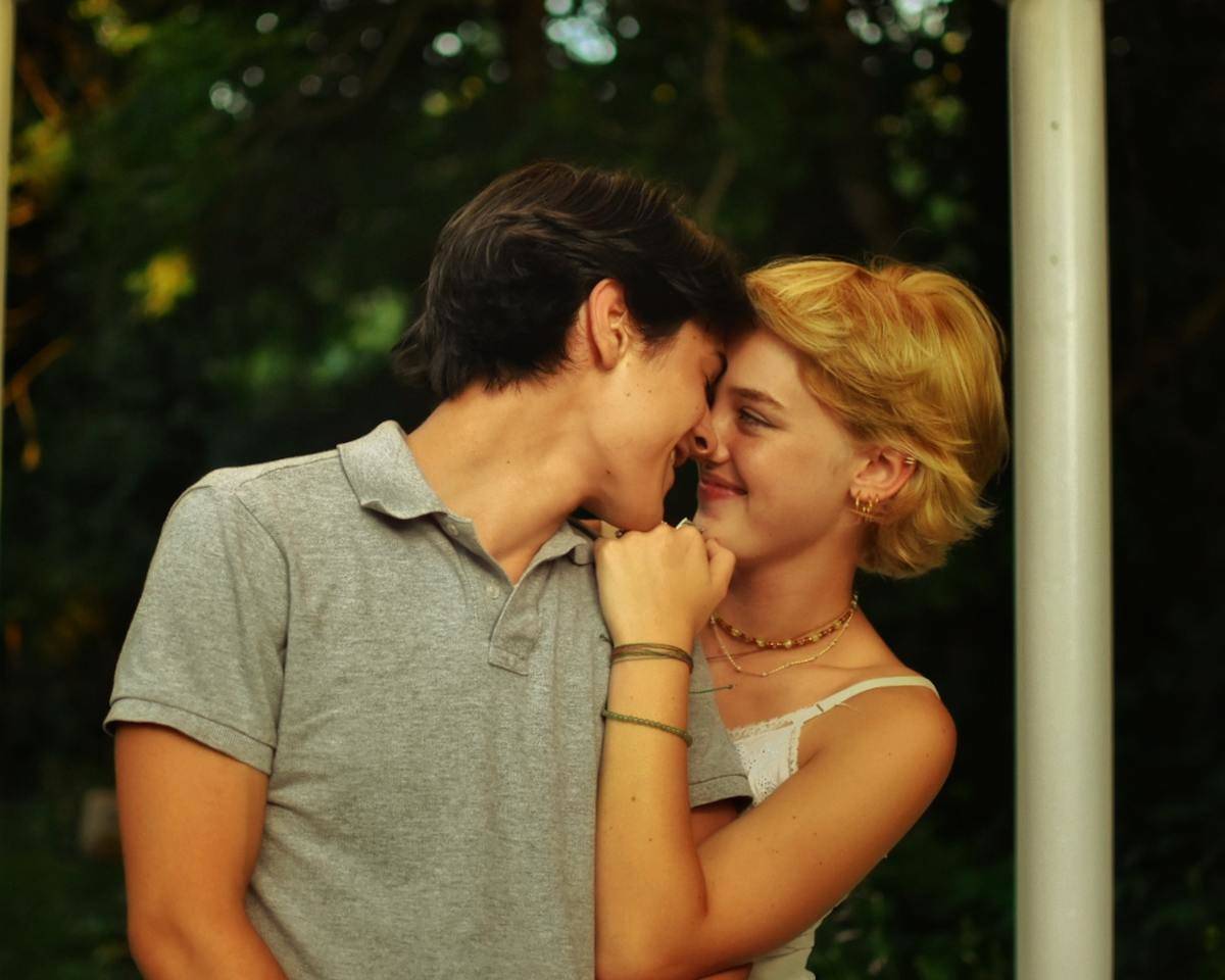 A boy with brown hair and a girl with blonde hair smiling in each other's faces.