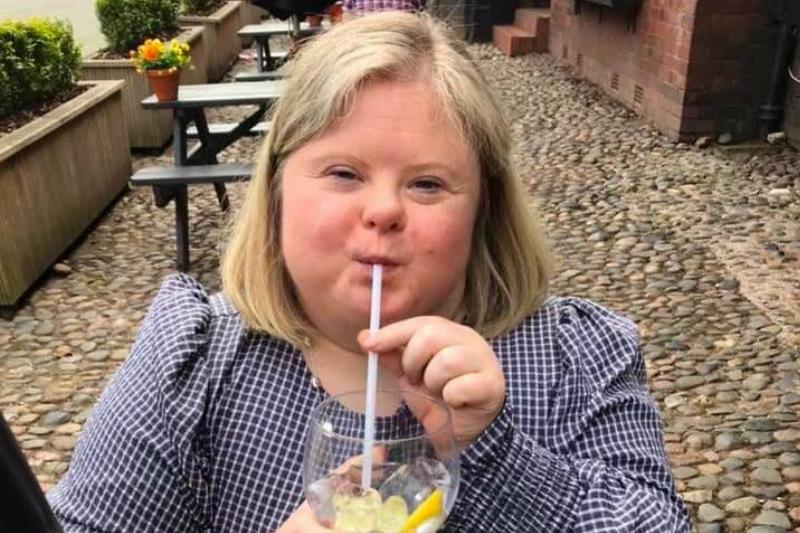 A woman with down syndrome sipping a drink at a restaurant.