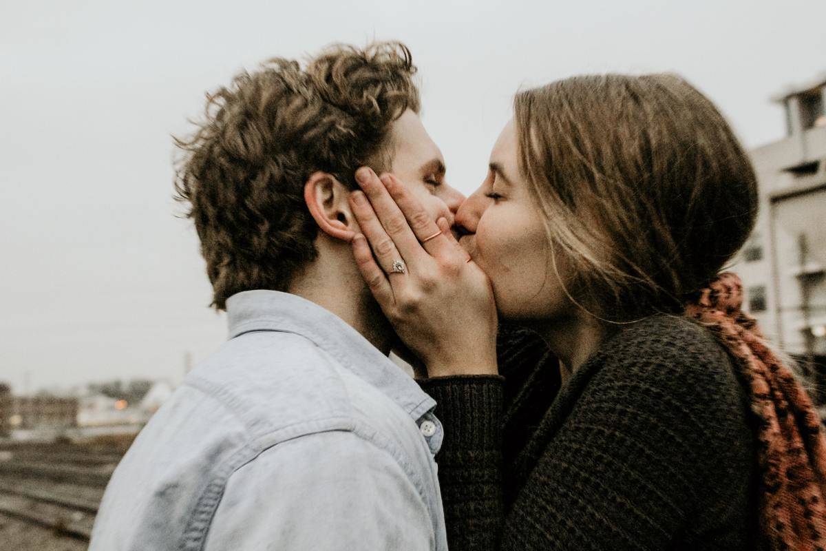 A young man and woman kissing, the girl holding his face in her hands.