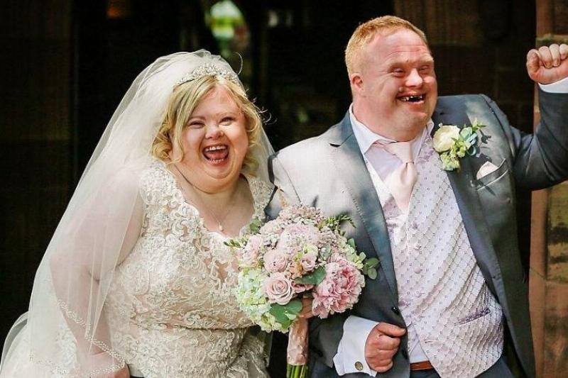 A man and woman with down syndrome leaving their wedding ceremony with smiles on their face.