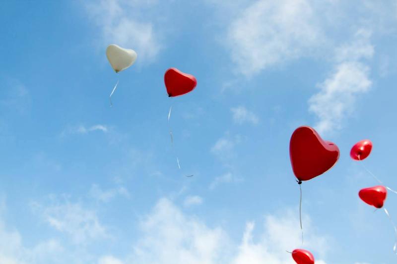 White and red heart-shaped balloons floating in a cloudy blue sky.
