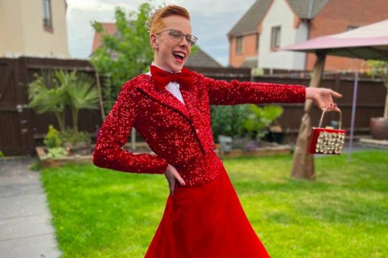 A man posing in a sparkly red prom outfit with a big smile on his face.