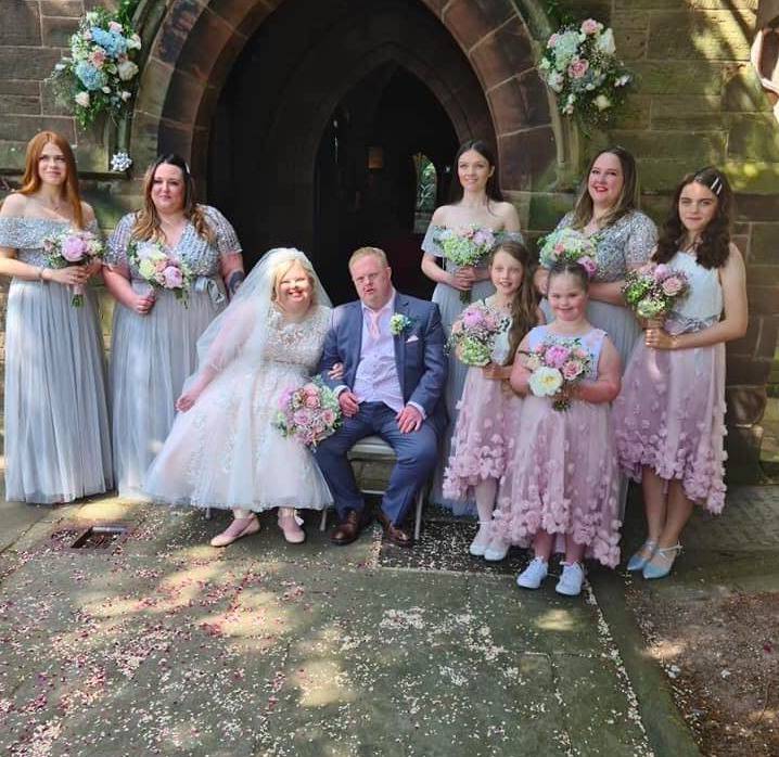 A couple with down syndrome getting married, with bridesmaids and flower girls surrounding them.