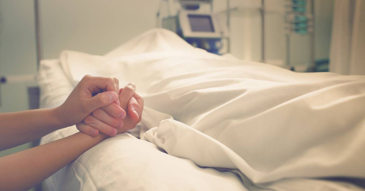 holding hands with person under blanket in hospital bed