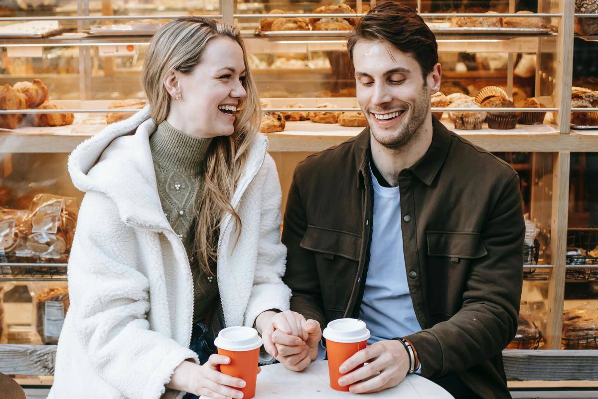 cheerful-young-couple-holding-hands-during-date-in-bakery