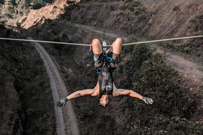 man hangs upside down off rope between too cliffs over road