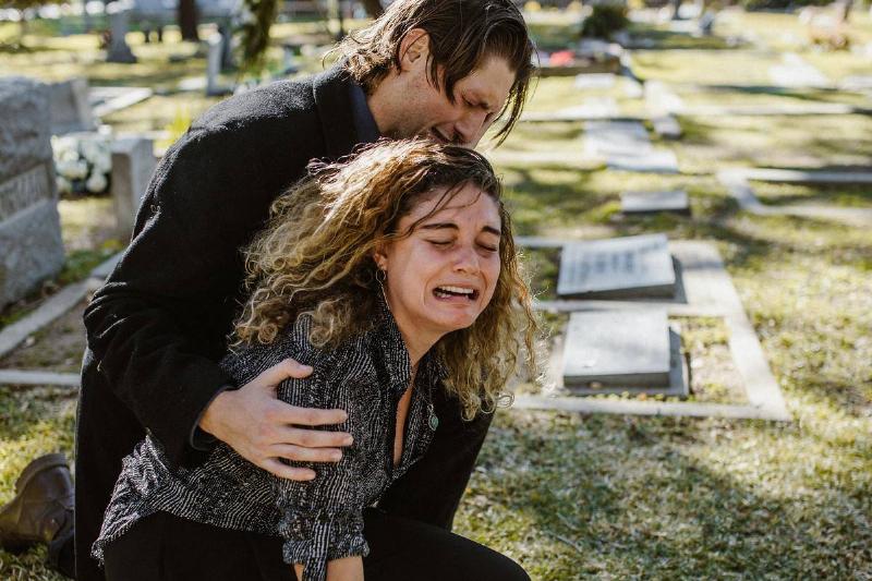 woman cries at cemetery while comforted by other crying man