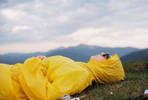 woman laying in yellow jacket on hill