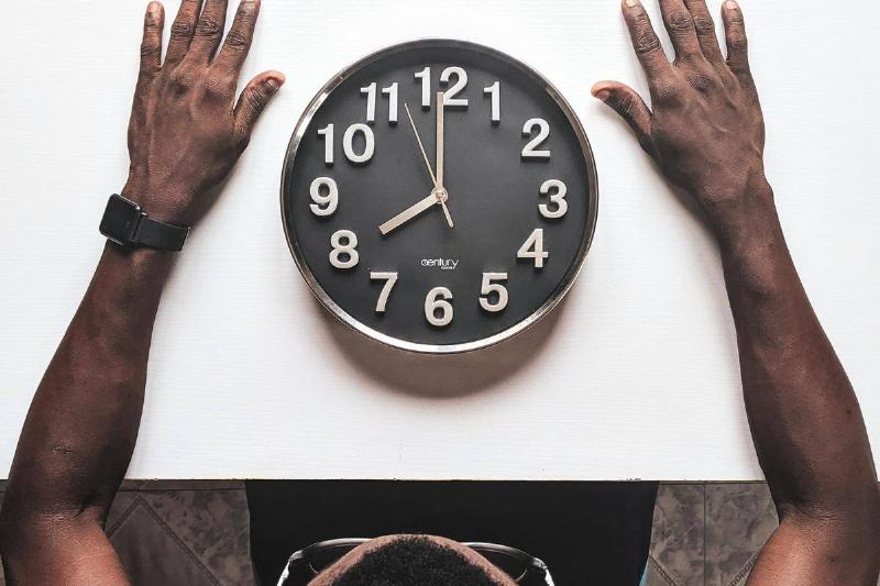 man puts his hands sitting around a round-silver-colored-wall-clock