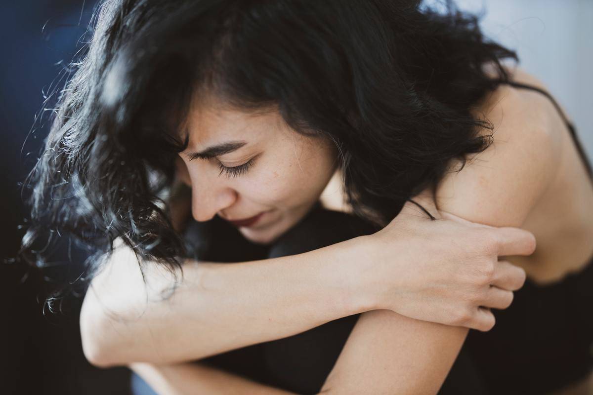 sad woman-wearing-black-camisole hugging in her knees