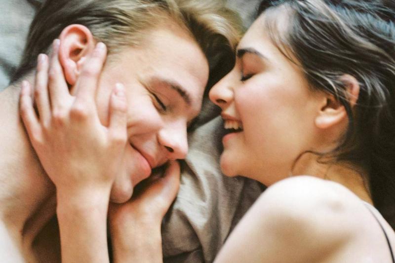 woman holds man's face close in bed as they both smile with eyes closed