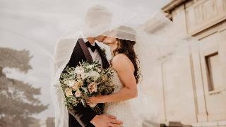 an-and-woman-kissing as bride ad groom under veil holding bouquet