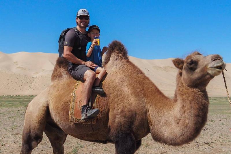 Youngest son drinks juice on camel with dad