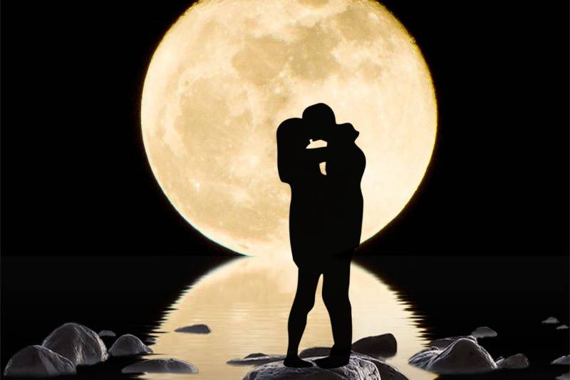 silhouette of couple embrace  standing on a rock under giant yellow moon