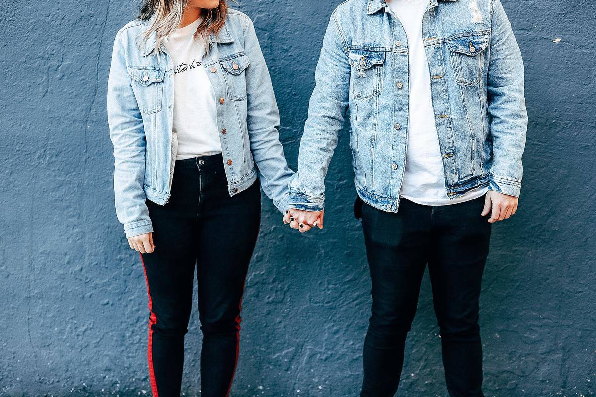 wo-person-standing-and-holding-their-hands-beside-blue-wall-both wearing denim jackets