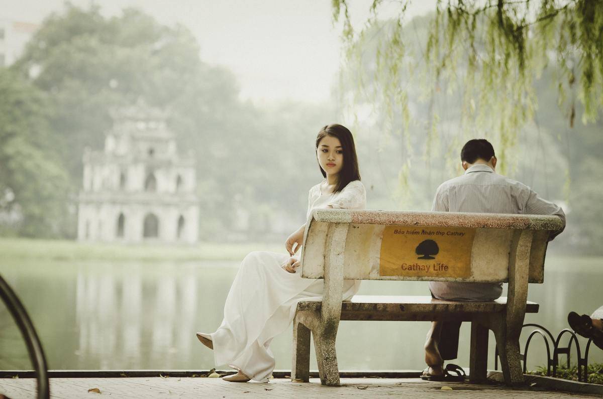 woman-sitting-on-bench-outdoors facing opposite side from man