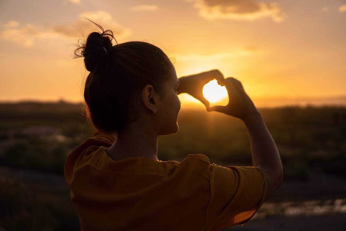 woman-doing-hand-heart-sig framing the sun within it