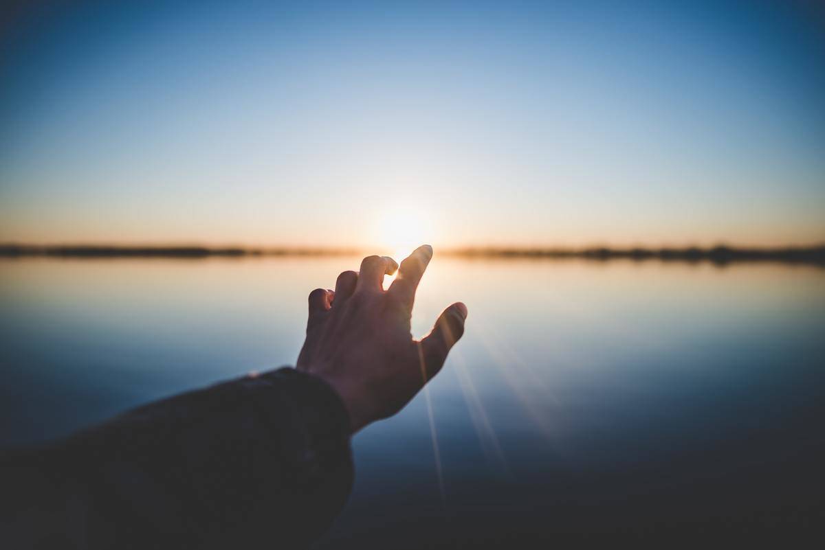 hand reaching for sun over the lake
