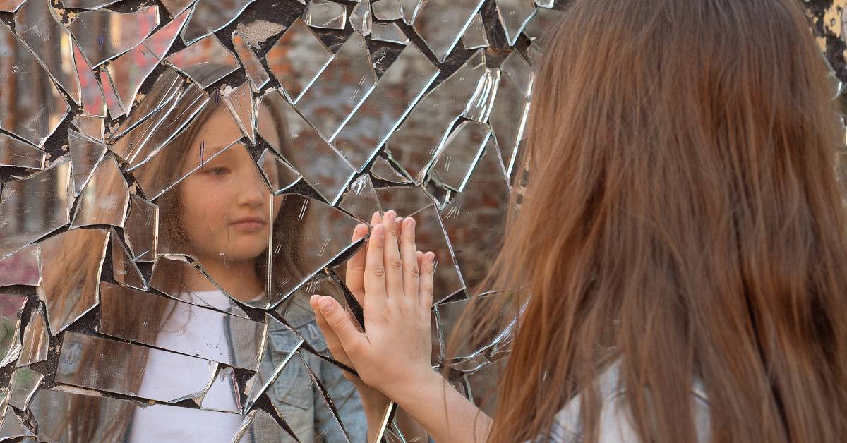 young girl looking at her reflection in shattered mirror