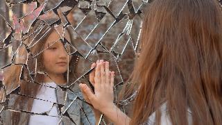 young girl looking at her reflection in shattered mirror