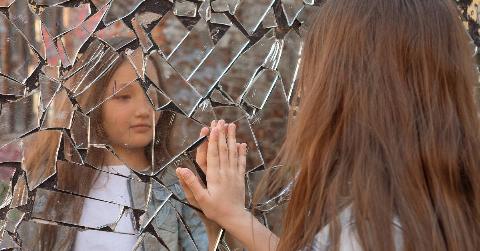 young girl looking at her reflection in shattered mirror