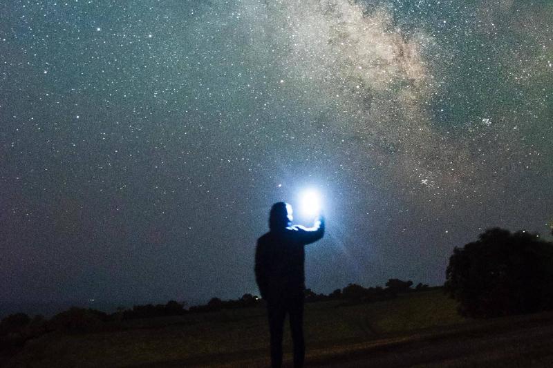 man holding white light to starry sky constellation