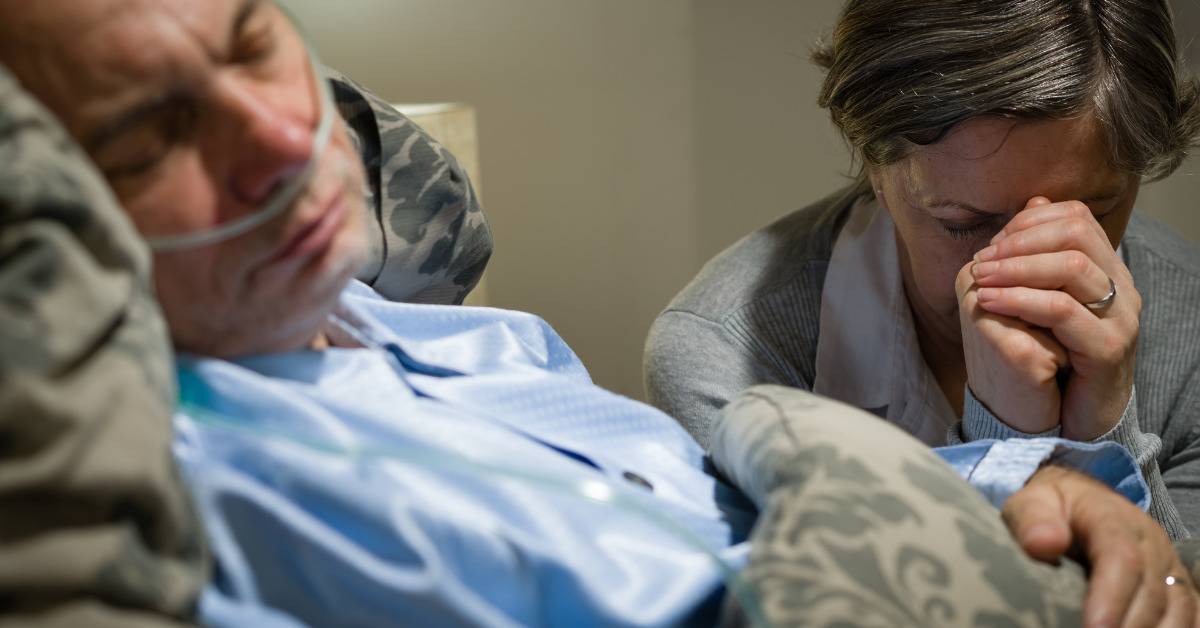 man in hospital gown with respirator beside crying woman praying